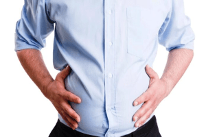 Motilidad intestinal - Hombre con camisa azul tocándose el abdomen inflamado, síntoma de motilidad intestinal