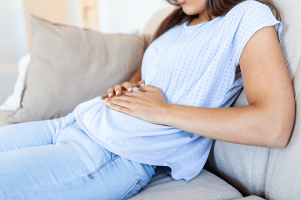 Motilidad intestinal - Mujer sentada en el sofá, tocándose el abdomen con dolor, indicando posibles problemas estomacales