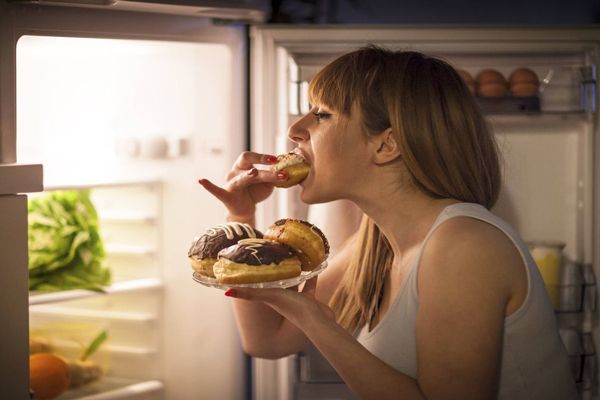 Mujer comiendo en exceso frente a la nevera. 