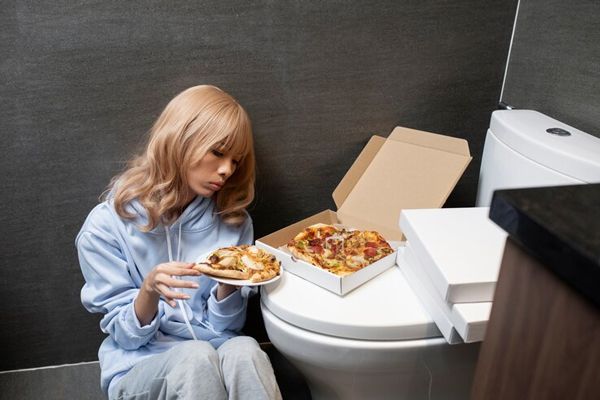 anorexia y bulimia- Chica rubia con trastornos alimenticios dandose un atracón de comida en el baño