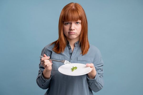 chica pelirroja con trastornos alimenticios, con un plato casi vacio frente a ella