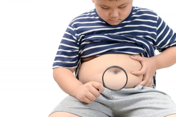 Niño obeso mirando su abdomen con una lupa