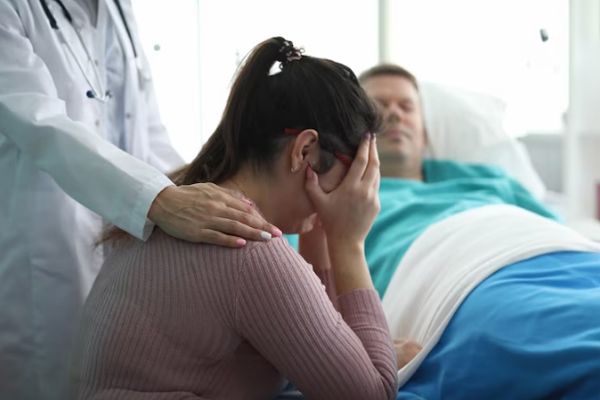 mujer llorando al lado de hombre tendido en una cama de hospital