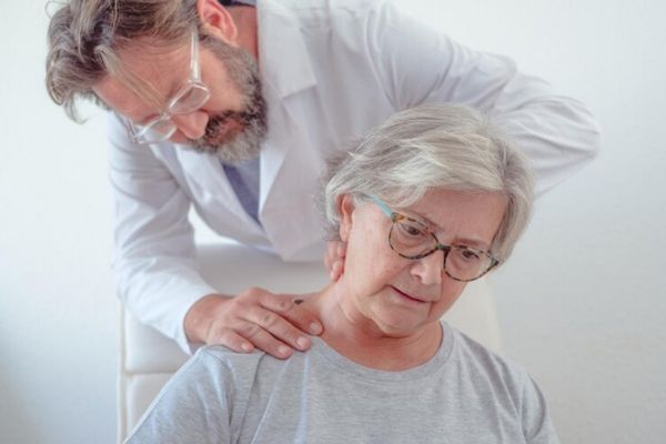 Médico le hace un examen físico a adulta mayor con dolor cervical
