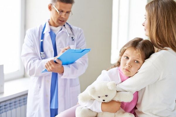 Médico revisando a niña sobre el regazo de su madre