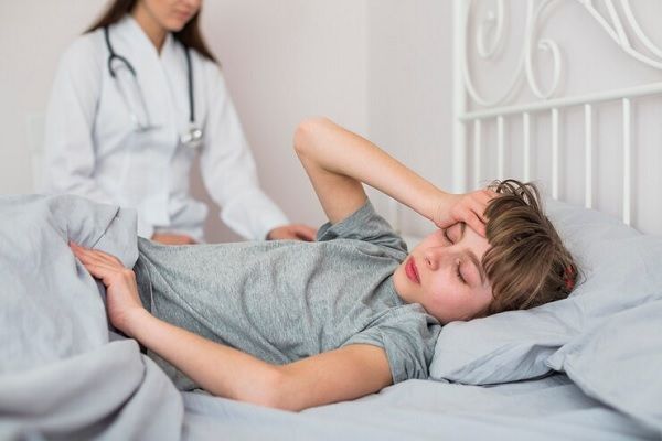 Niño recostado en una cama, presionando su cabeza con la mano