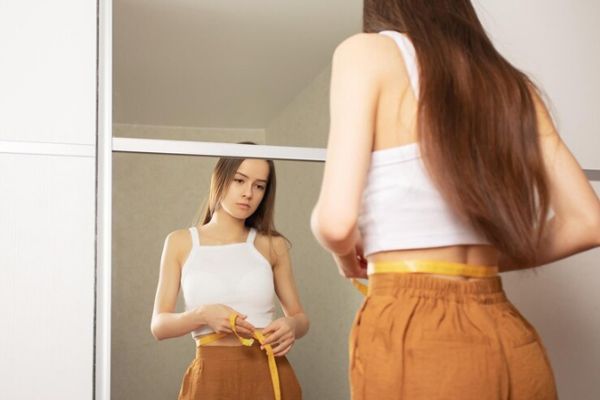 Tipos de trastornos alimenticios - Joven midiendo su cintura frente al espejo
