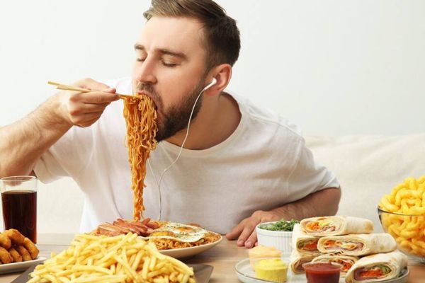 Tipos de trastornos alimenticios - hombre jovén ingiriendo un atracón de comida