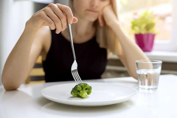 Tipos de trastornos alimenticios - Mujer joven a dieta comiendo brócoli