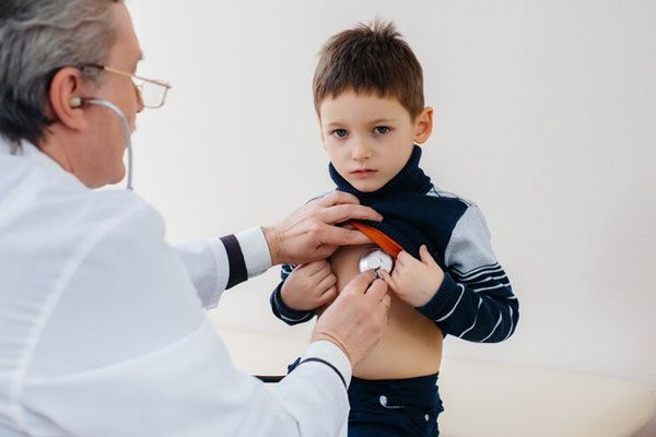 Cardiólogo escucha y examina con detenimiento los latidos cardíacos de un niño
