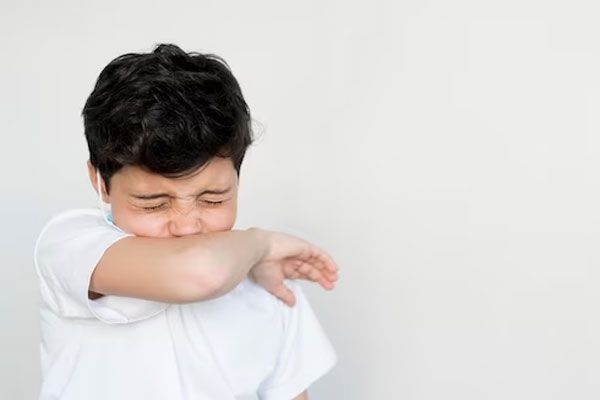 Varicela y sarampión - Niño con camisa blanca estornuda contra la parte interior del codo para no esparcir bacterias en el aire