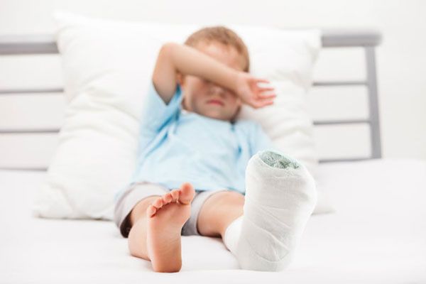 Osteogénesis - Niño con fractura en el pie se tapa la cara mientras reposa sobre la cama