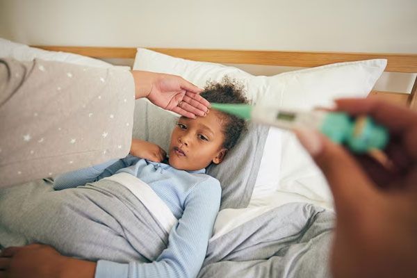 Sarampión - Madre le toma la temperatura a un niña en cama para controlar los niveles de fiebre