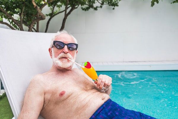 Adulto mayor con lentes toma sol en una silla junto a la alberca