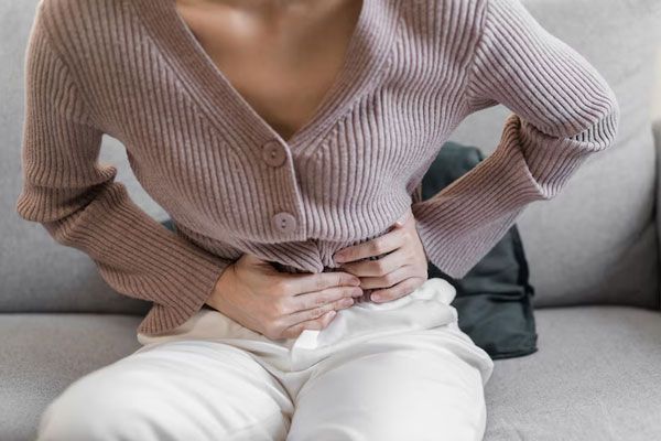 Enfermedad inflamatoria pélvica - Joven se sienta sobre el sofá tras percibir un agudo y repentino dolor en la parte baja del abdomen