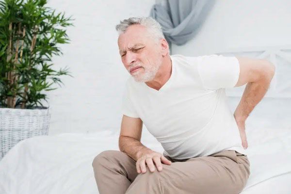 Adulto mayor se lleva las manos a la espalda ante persistente dolor en el coxis 