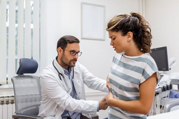 Tipos de hepatitis - Doctor examina a una paciente en su consultorio tras presentar un persistente dolor abdominal