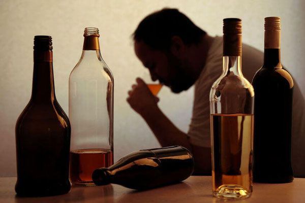 Hombre con problemas de alcoholismo y botellas de fondo