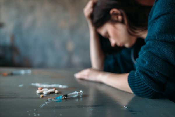 Drogadicción - Mujer con problema de adicción a las drogas, sintiéndose abrumada sobre una mesa con varias sustancias narcóticas