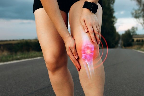 Mujer con un fuerte dolor en la rodilla mientras realiza ejercicio, como consecuencia de la bursistis que padece