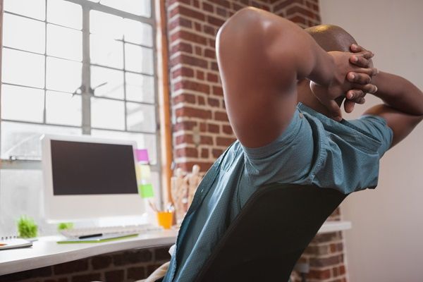 Hombre estirándose mientras trabaja sentado frente a la computadora, como medida de tratamiento para tener una postura adecuada