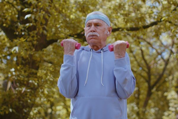 Hombre de avanzada edad realizando ejercicios de peso, los cuales ayudan a fortalecer los huesos