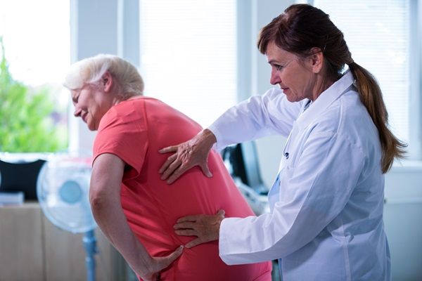 Qué es la osteoporosis - Doctora realizando un diagnóstico a una mujer mayor con dolor en la espalda, para determinar si sufre de osteoporosis