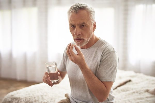 Hombre mayor tomando medicamentos, para aliviar los dolores causados por la afección esquelética que padece