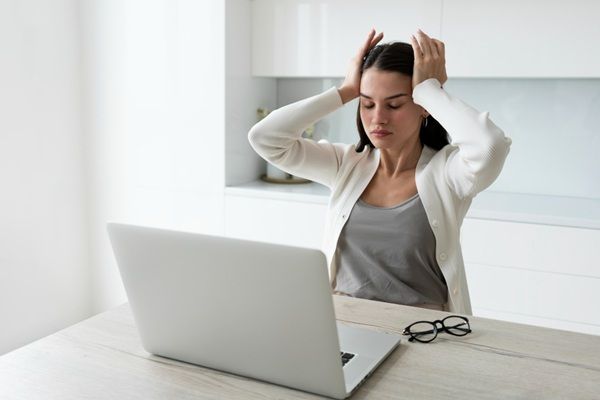 Enfermedades actuales - Mujer usando una computadora con mucho estrés que causa enfermedad y evita mantenerte saludable, siendo una de las enfermedades actuales más comunes