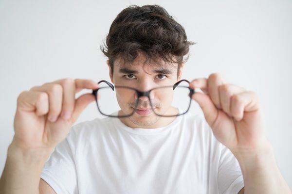 Miopía y astigmatismo - Hombre sosteniendo gafas para miopía y astigmatismo que ayudan a solucionar los problemas de visión borrosa