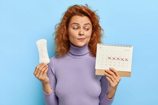 Síntomas del embarazo - Mujer sosteniendo un calendario observando el atraso menstrual que presenta como parte de los primeros síntomas del embarazo